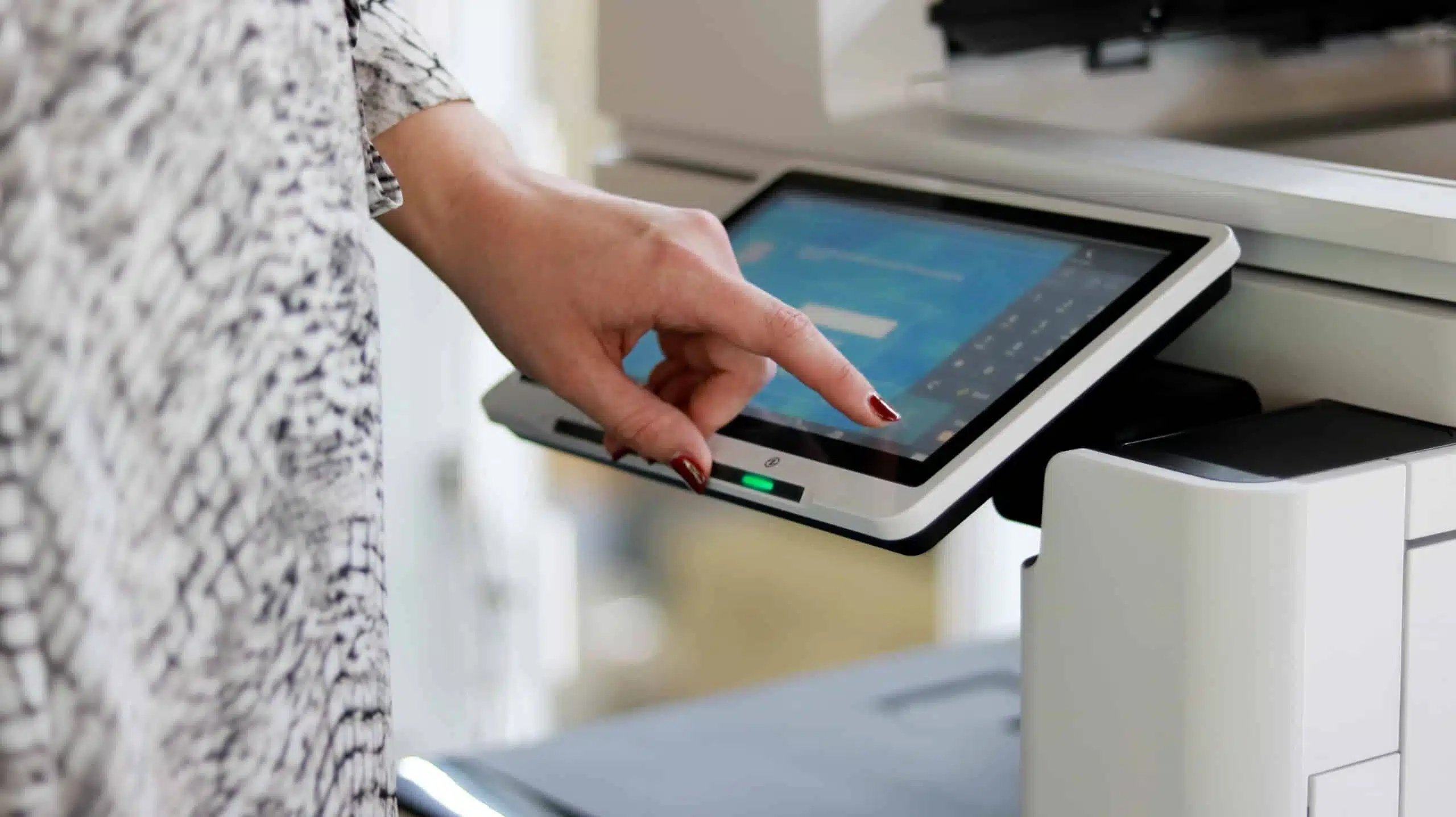 Een hand bedient het touchscreen van een printer of copier — een intuïtieve interface als onderdeel van onze printoplossingen.
