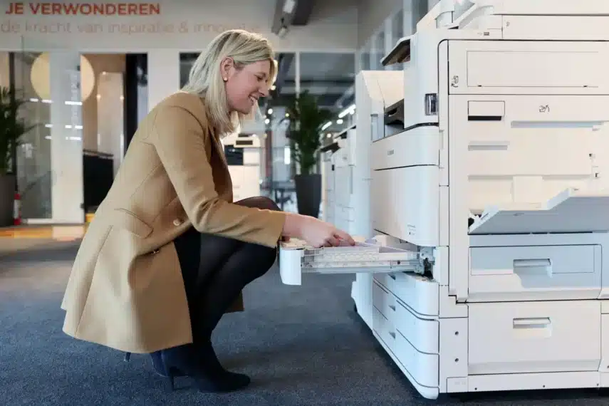 Vrouw vult papier bij in een moderne Canon kopieermachine op kantoor – kopieermachine leasen.