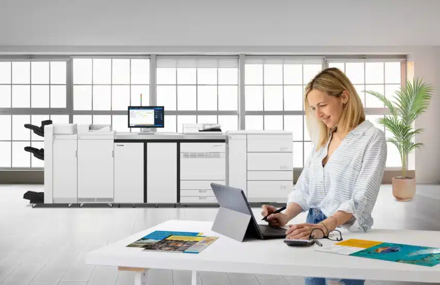 Professioneel kopieerapparaat in moderne kantoorruimte naast medewerker die werkt aan documenten.