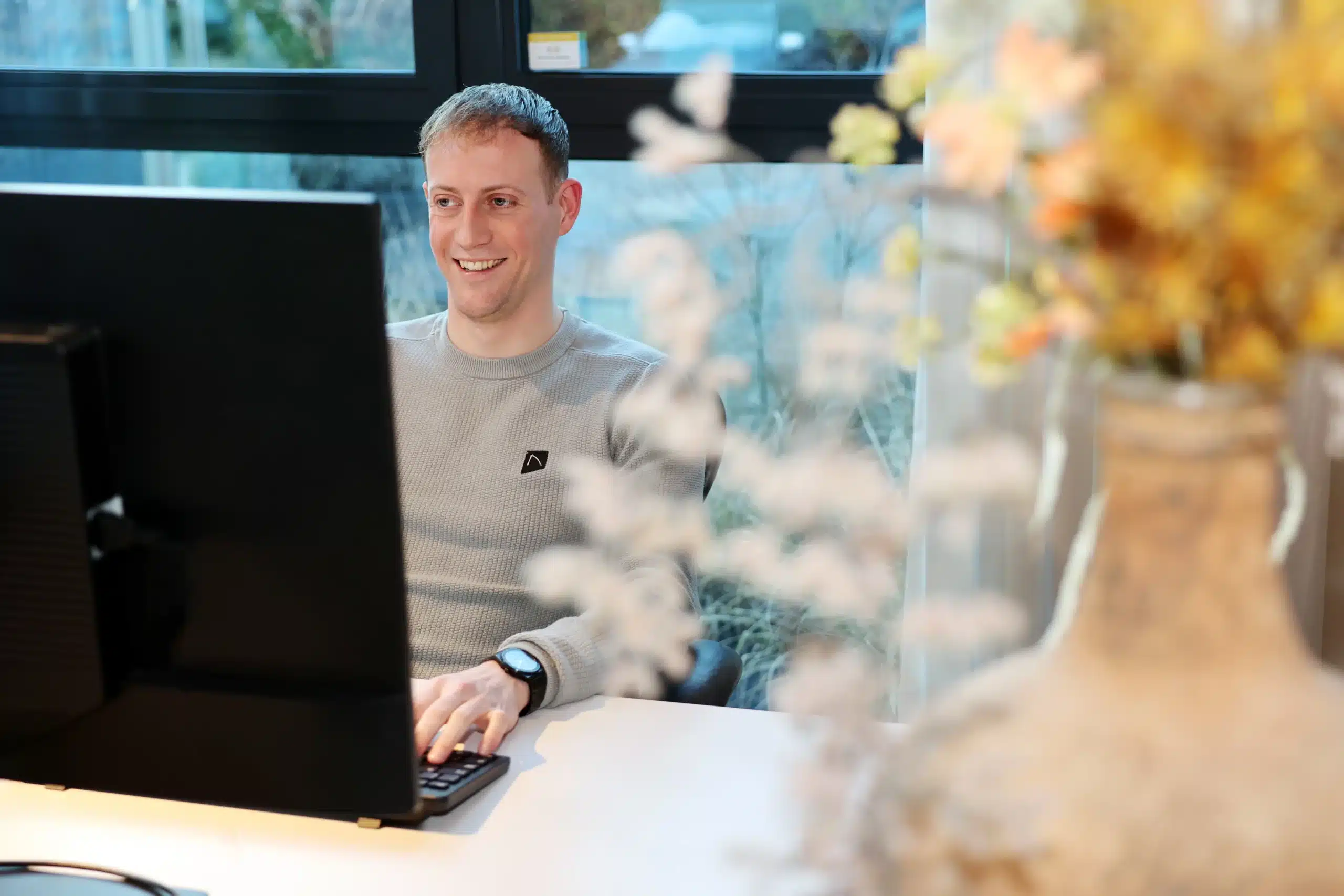 Medewerkersverhaal Tomas Baljeu – medewerker achter bureau werkt geconcentreerd op computer in een moderne kantooromgeving.