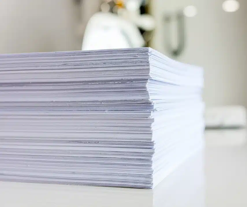Close-up van een grote stapel wit papier op een bureau, verwijzend naar papierverbruik en de noodzaak van duurzaam printen.