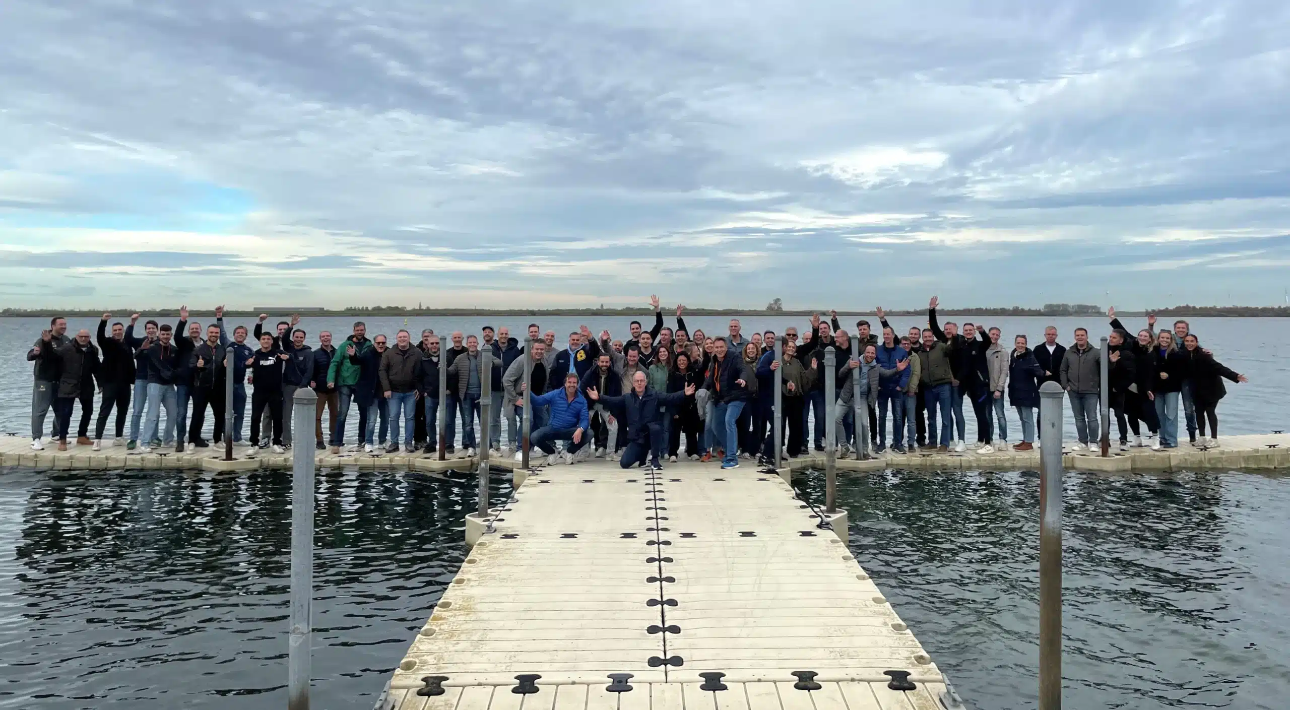 Ontdek onze cultuur tijdens de Mega Medewerkers Getaway met een grote groep collega’s op een steiger aan het water.