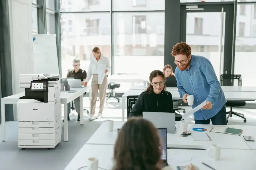 Multifunctionele kantoorprinter in een open kantoorruimte waar ongeveer 25 medewerkers samenwerken.
